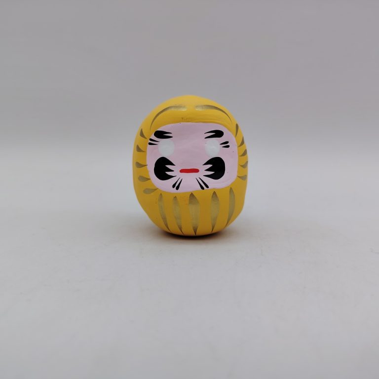 Bambola Daruma gialla tradizionale giapponese, vista frontale con dettagli del volto stilizzato e corpo tondeggiante