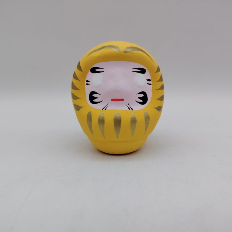 Bambola Daruma gialla tradizionale giapponese, vista frontale con dettagli del volto stilizzato e corpo tondeggiante