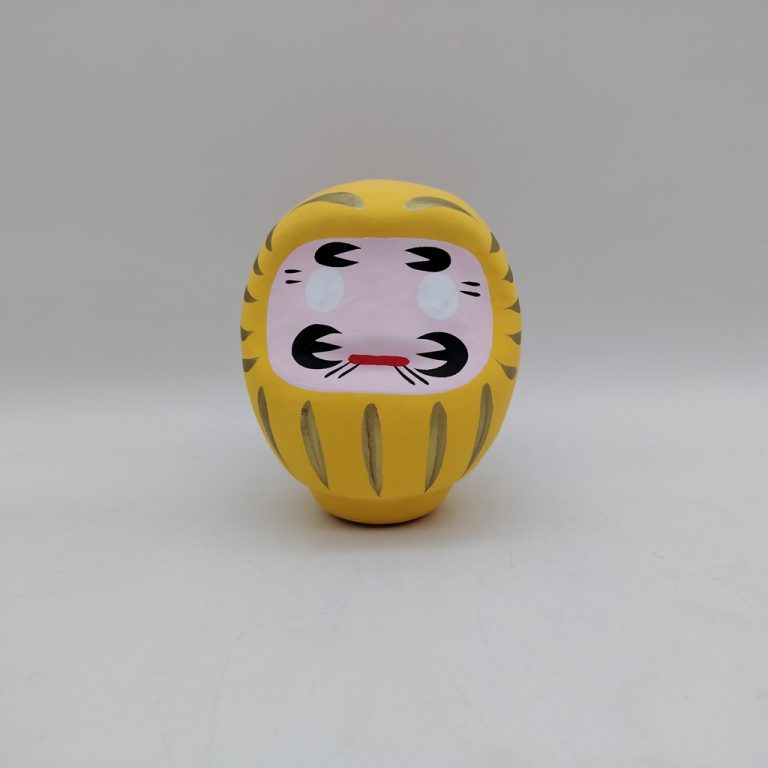 Bambola Daruma gialla tradizionale giapponese, vista frontale con dettagli del volto stilizzato e corpo tondeggiante