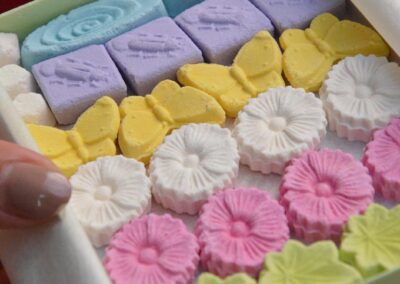 A green box full of cookies decorated in the shape of flowers and butterflies of various colors, held by a hand with pink nail polish.