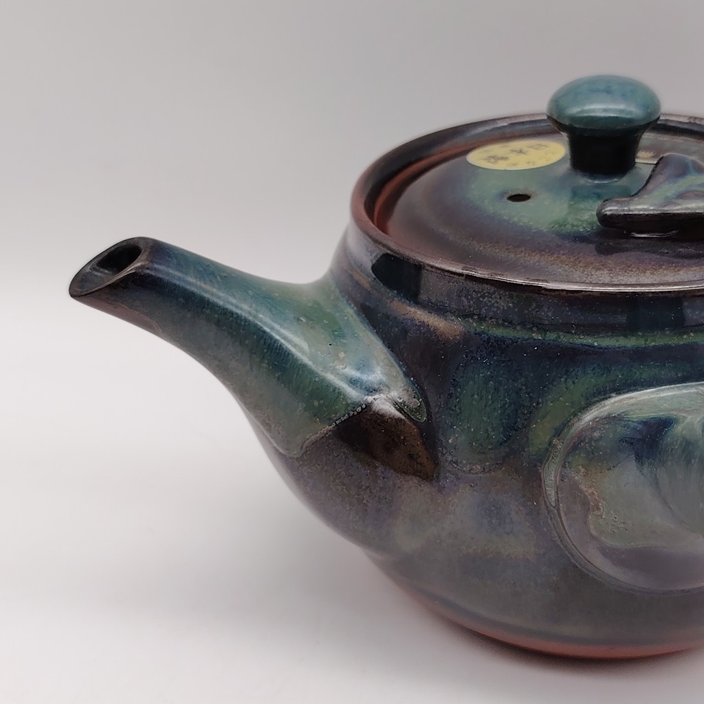 Kyusu in ceramica verde con fogliolina, 380ml, con finitura iridescente che riflette toni di blu e marrone. Il tappo è decorato con una piccola foglia.