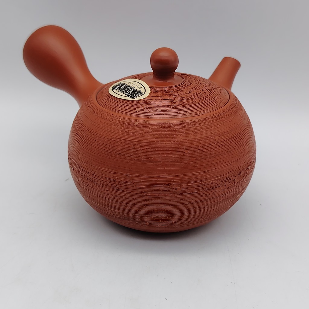 Tè Kyusu rossa "matsukawa" con capacità di 180 ml, raffigurante un motivo a spirale, con un'etichetta bianca su fondo marrone. Posizionato su una superficie bianca.