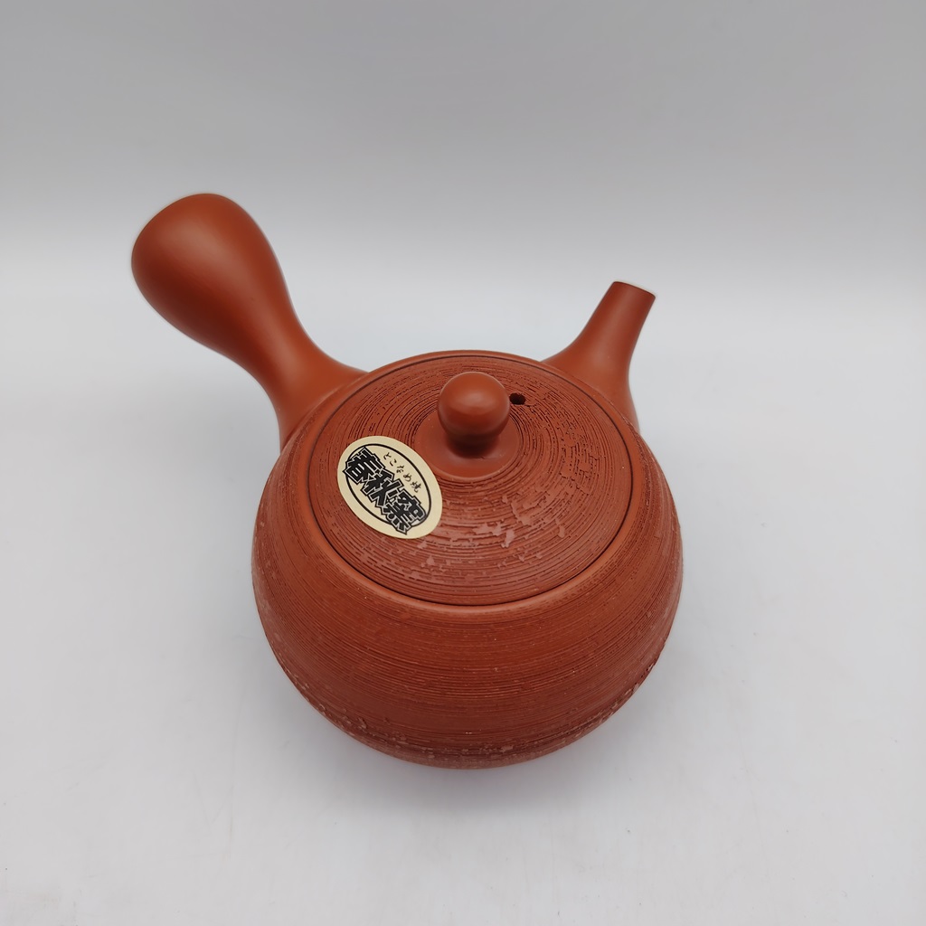 Una teiera rossa "matsukawa" da 180ml, con un manico curvo e un tappo rotondo, con un'etichetta in bianco e nero sulla superficie, su sfondo bianco.