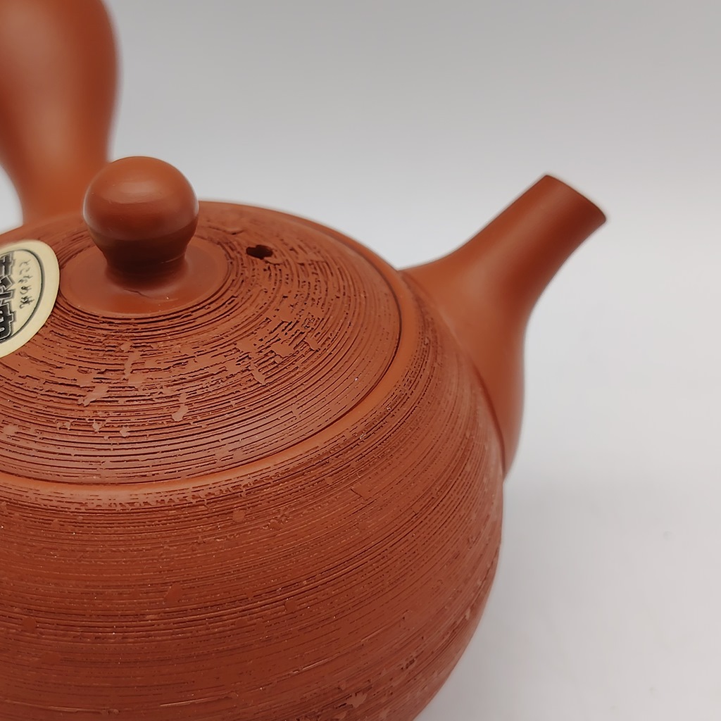 Kyusu rossa "matsukawa" da 180ml in terracotta, con texture a righe e tappo rotondo. Una piccola etichetta con testo giapponese è visibile sul coperchio.