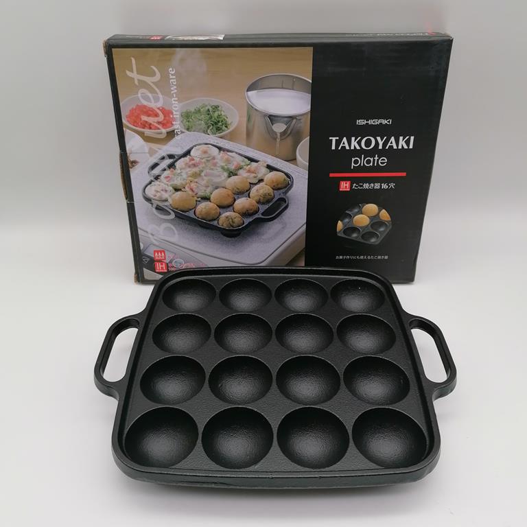 Padella per takoyaki in ghisa ISHIGAKI a 16 fori, nera, con scatola e utensili da cucina in primo piano.