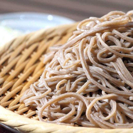 Un primo piano di zaru soba, un piatto di spaghetti di grano saraceno freddi serviti su un cestino di bambù, pronti per essere intinti in una salsa.