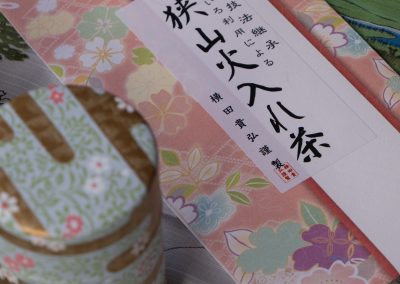 A traditional Japanese gift with paper gift wrap decorated with floral motifs and a three-layer tin can with a golden lid, placed on a surface with a striped fabric.