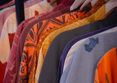 Colorful Japanese kimono hanging on a rod, with floral and geometric patterns in bright shades like orange, blue, and purple, arranged on a dark blue shelf.