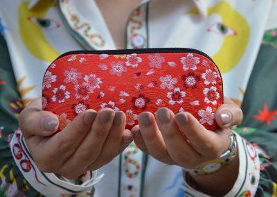 A woman in a long-sleeved shirt printed with colorful patterns is holding a red bag decorated with white flowers.