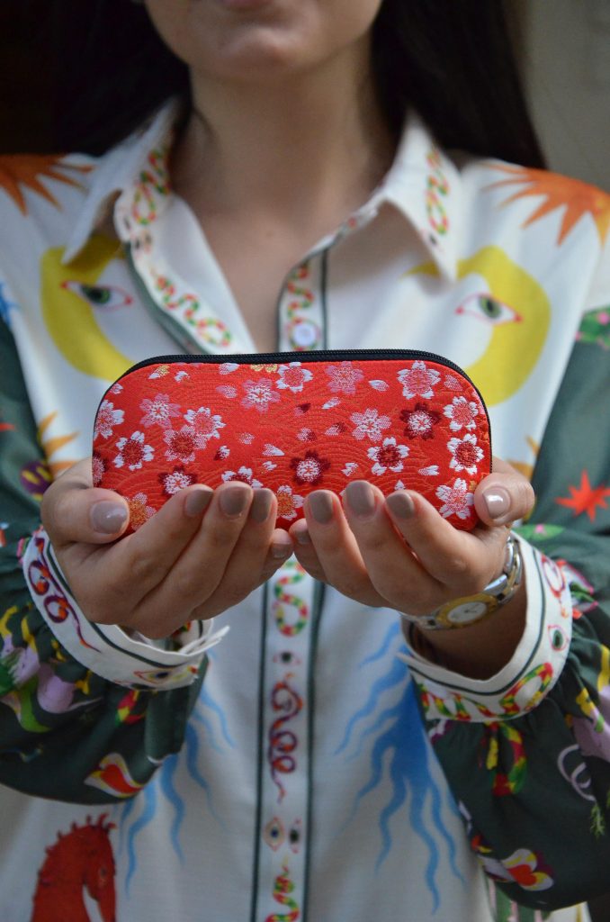 Una donna con una camicia a maniche lunghe stampata con motivi colorati sta tenendo una borsa rossa decorata con fiori bianchi.