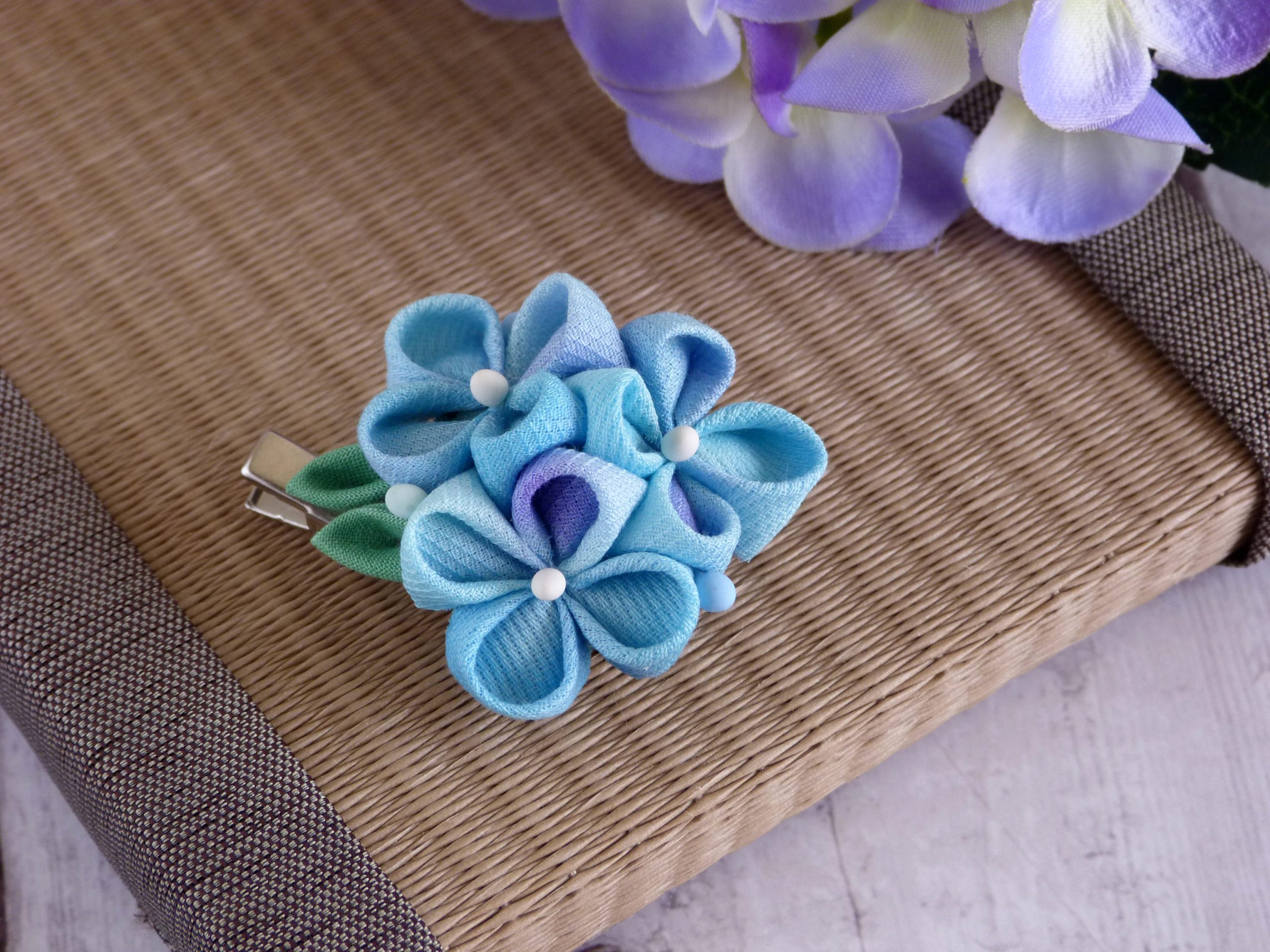 Fioritura azzurra di ortensia in seta con perline bianche su sfondo marrone, laboratorio Tsumami Zaiku.