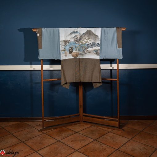 Haori vintage da uomo in seta marrone-grigio con il monte Fuji e strumenti per la cerimonia del tè, appeso su un'asta di legno marrone su uno sfondo blu.