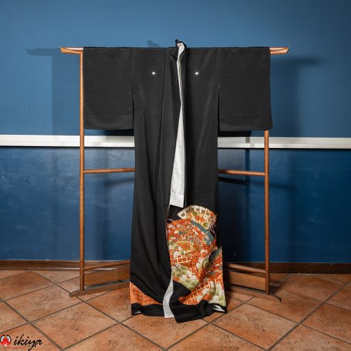 Kimono Kurotomesode vintage in seta nera con pini e ventagli, appeso su un'asta di legno marrone su sfondo blu.