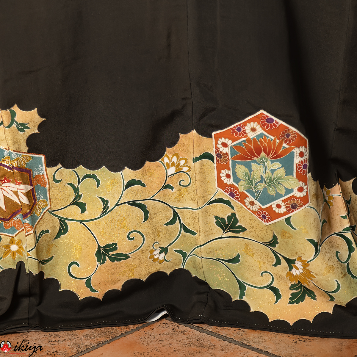 Primo piano di un kurotomesode vintage in seta nera con un elaborato motivo floreale e esagonale giallo e rosso, che mette in risalto fiori di loto e foglie stilizzate.