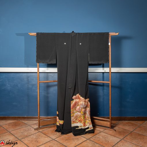 Kurotomesode vintage in seta nera con motivo shippo e dettagli floreali colorati, appeso su un cavalletto di legno davanti a uno sfondo blu.