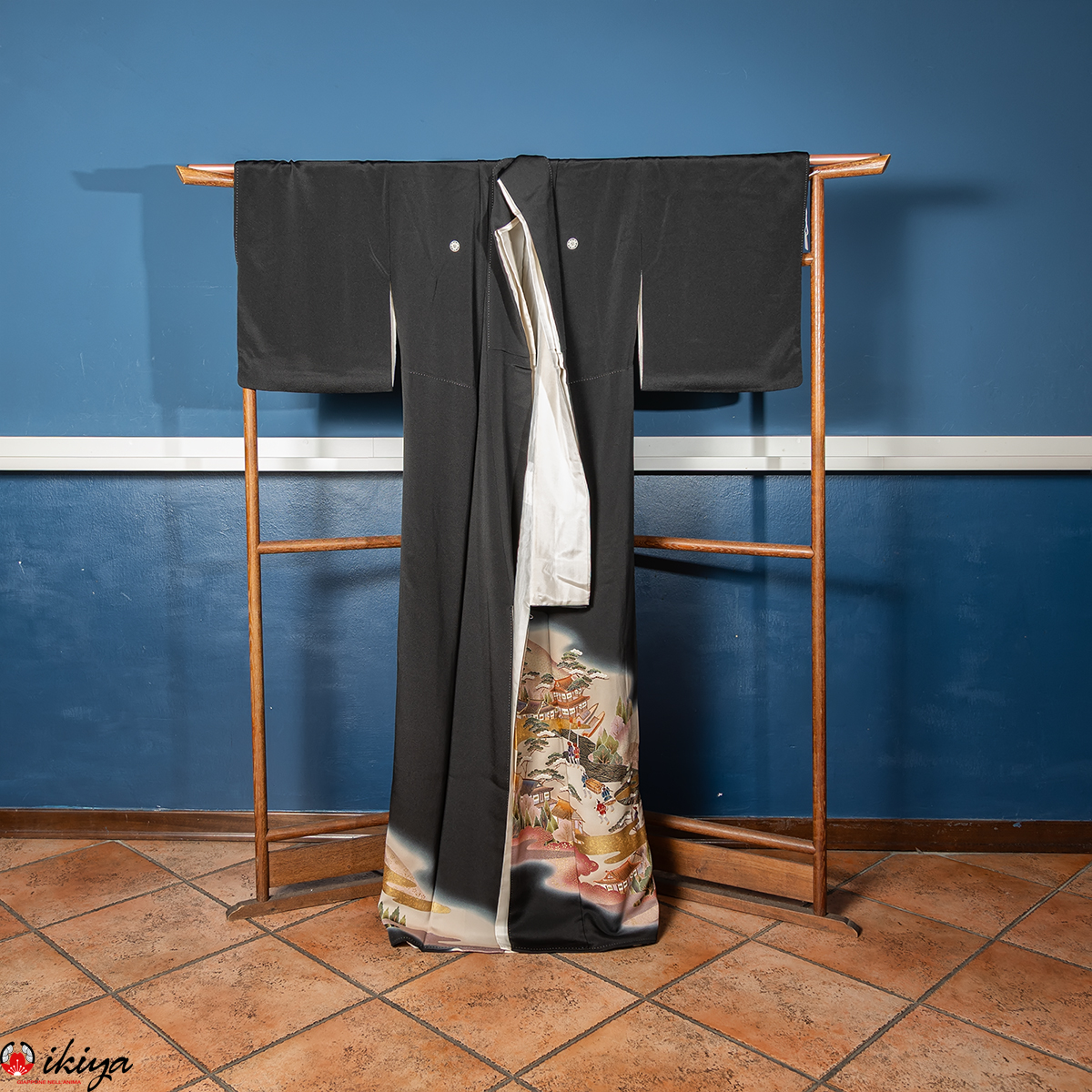 Kimono Kurotomesode vintage in seta nera con paesaggi e scene d’epoca Edo, appeso su un'asta di legno marrone su sfondo blu.
